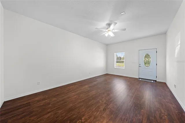a view of an empty room with wooden floor and a ceiling fan