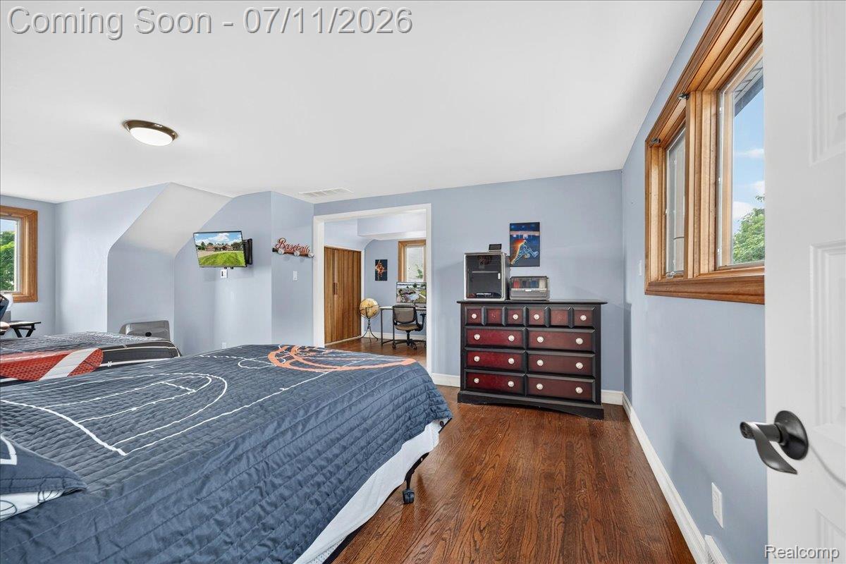 23750 East River Road Grosse Ile, MI 48138 - Photo 23 of 54 Bedroom featuring wood-finish flooring, light blue wall paint, natural wood window trim, white baseboards, and a flush-mount ceiling light fixture