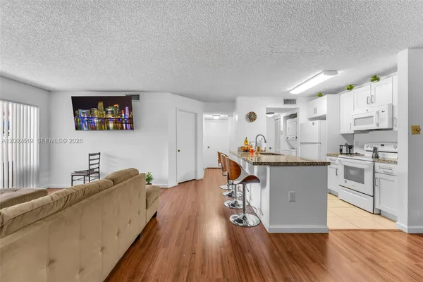 a living room with stainless steel appliances kitchen island granite countertop a couch a dining table and chairs with wooden floor
