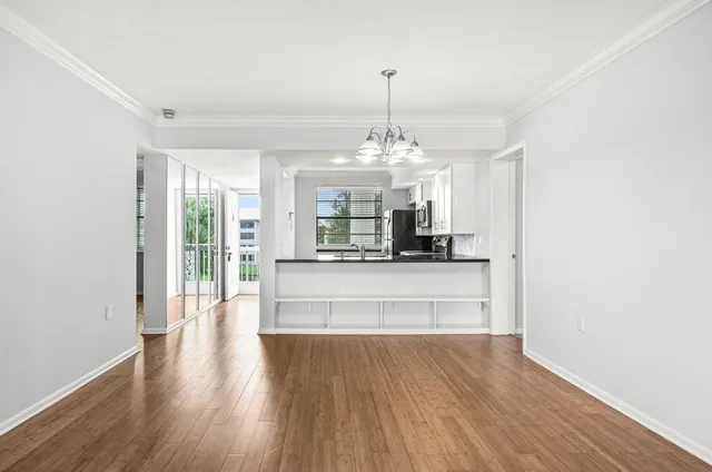 a view of an empty room and kitchen with wooden floor