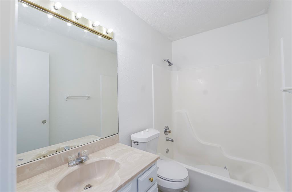 617 Rolling Ridge Court Azle, TX 76020 - Photo 9 of 20 Bathroom featuring a vanity with a drop-in sink and a light-colored countertop, an overhead vanity light with exposed bulbs, a large wall-mounted mirror, a toilet, and a combined shower-tub unit with a chrome showerhead