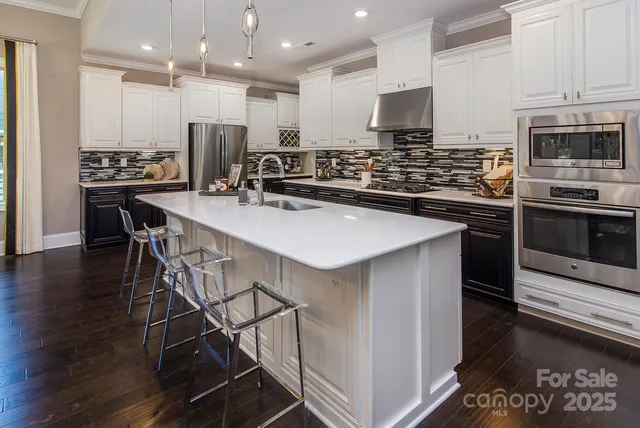 a kitchen with kitchen island stainless steel appliances a sink a stove a microwave a refrigerator and chairs