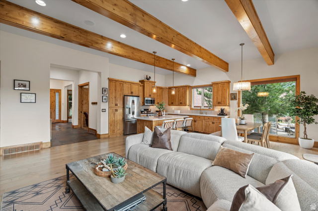 4892 Eagle Rdg Drive Eden, UT 84310 - Photo 6 of 39 Open-concept living space featuring vaulted ceilings with exposed wood beams, light wood-finish flooring, a contemporary kitchen with wood cabinetry and stainless steel appliances, a dining area with a modern chandelier, and large windows offering exterio