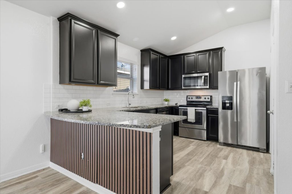 19040 Kimberlite Drive Pflugerville, TX 78660 - Photo 11 of 40 Kitchen with stainless steel appliances, a peninsula, dark cabinets, light stone countertops, and light wood-style floors