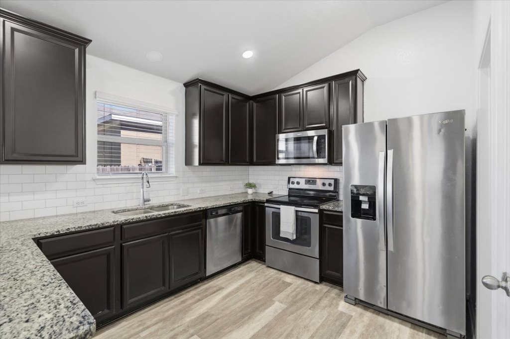 19040 Kimberlite Drive Pflugerville, TX 78660 - Photo 12 of 40 Kitchen with appliances with stainless steel finishes, light stone countertops, lofted ceiling, decorative backsplash, and light wood finished floors