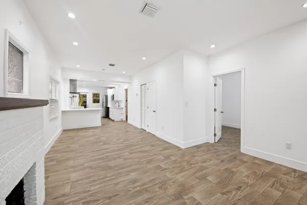 a view of an empty room with wooden floor and a kitchen