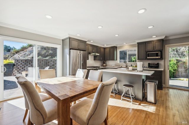 a dining room with stainless steel appliances a dining table wooden floor and a large window