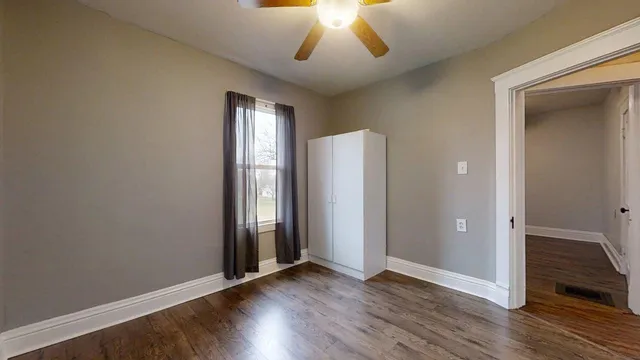 a view of an empty room with wooden floor and a window