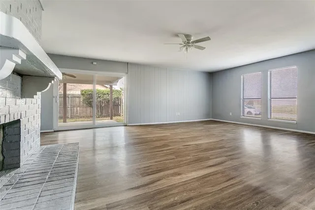 an empty room with wooden floor fan and windows