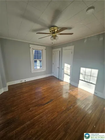 an empty room with wooden floor chandelier fan and windows