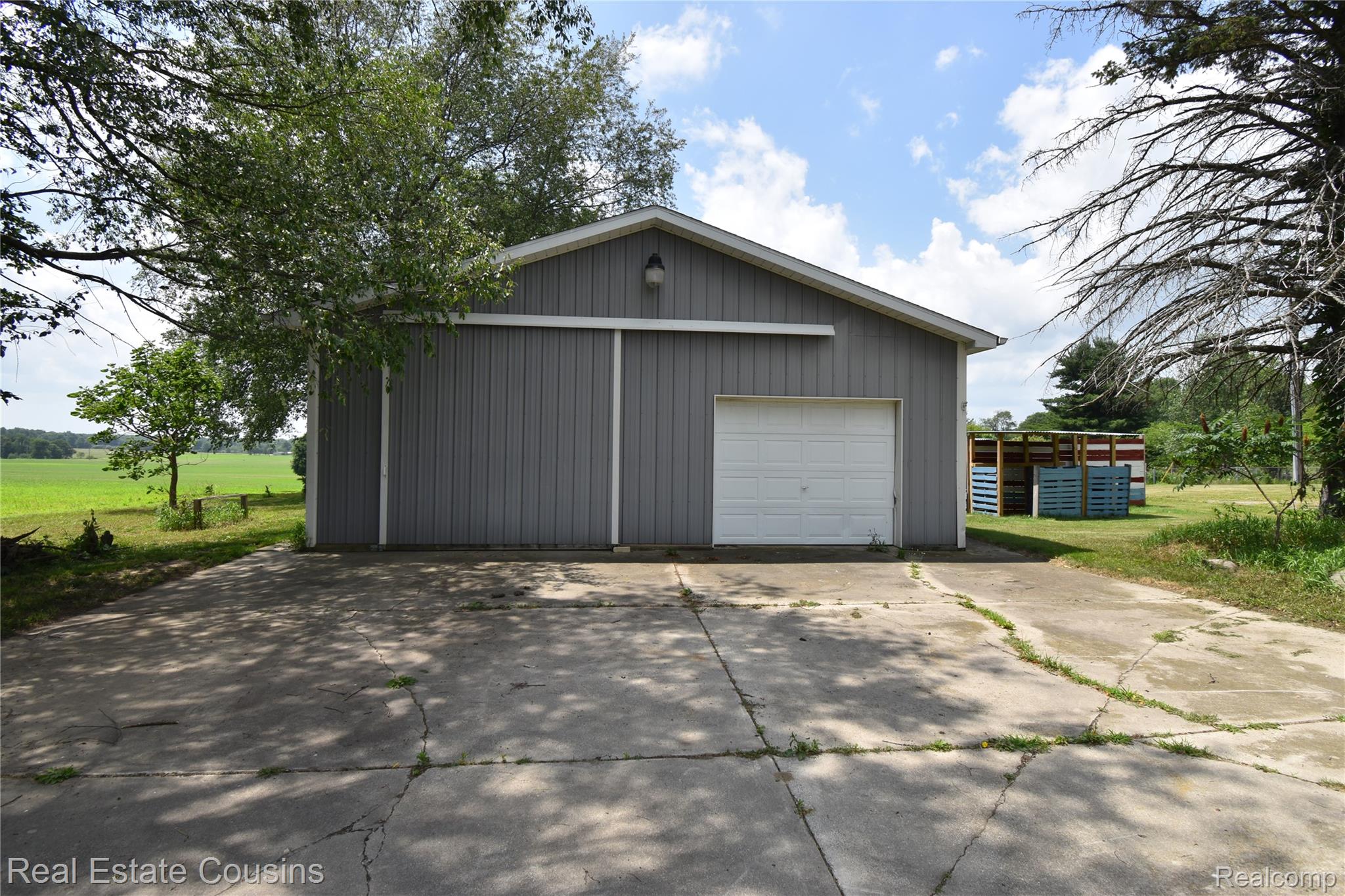2247 Johnson Mill Road North Branch, MI 48461 - Photo 18 of 22 Detached gray corrugated metal building featuring a white garage door, overhead lighting fixture, and a concrete driveway