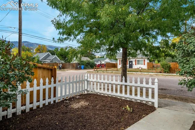 a view of a brick house with large trees and wooden fence