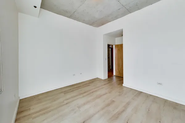 a view of an empty room with wooden floor and a bathroom