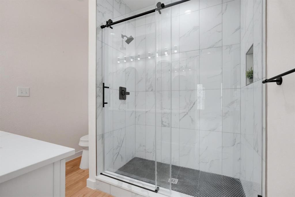 504 South O Connor Road Irving, TX 75060 - Photo 16 of 23 Modern shower enclosure featuring a glass sliding door with black hardware, white veined tile walls, and a black mosaic tile floor