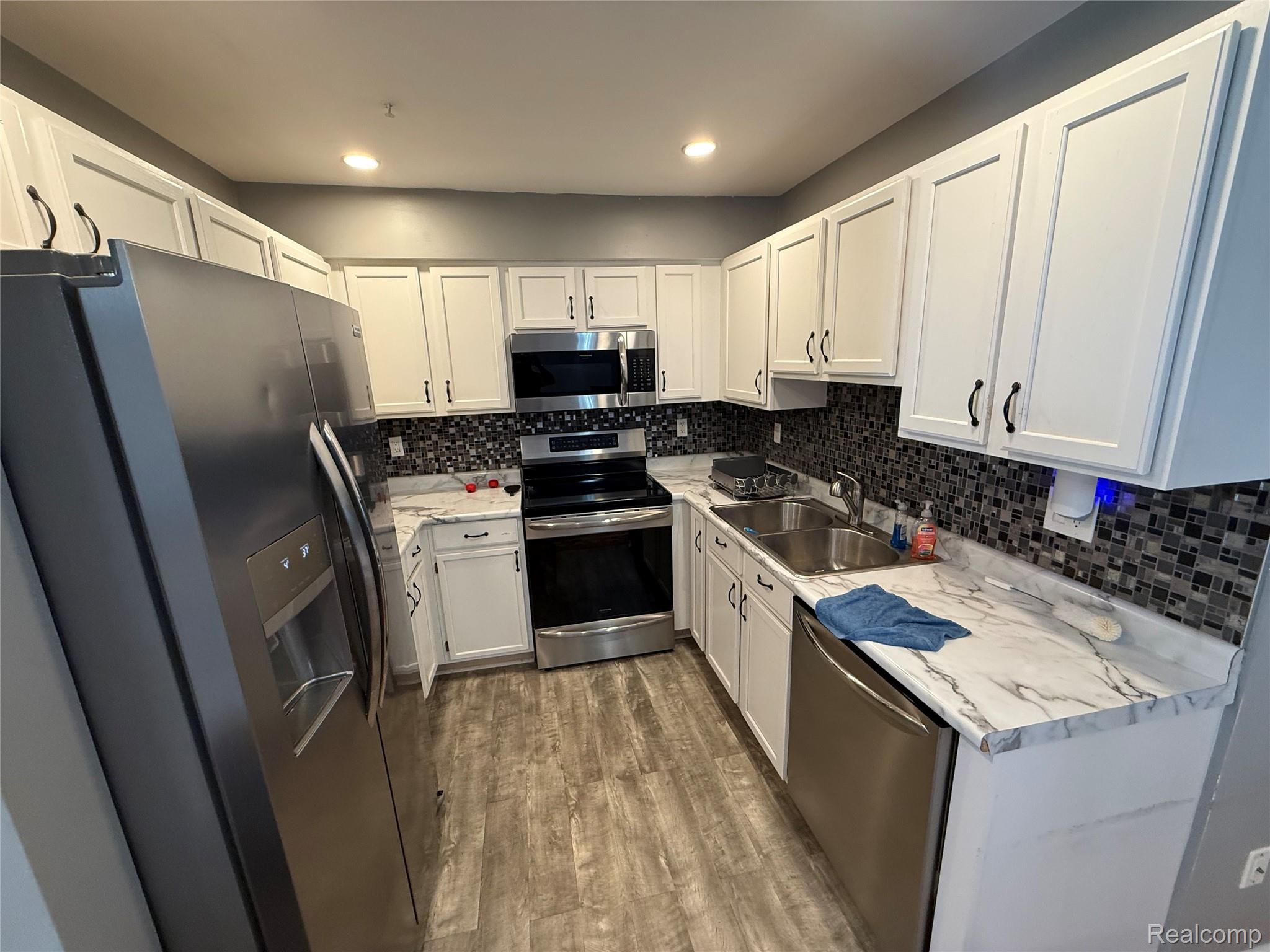 4308 Schaefer Road Dearborn, MI 48126 - Photo 9 of 11 Kitchen featuring white cabinetry, wood-finish flooring, stainless steel appliances, mosaic tile backsplash, and a double basin sink