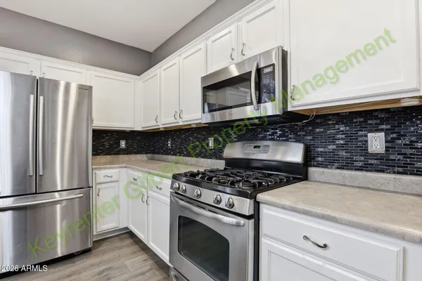 a kitchen with stainless steel appliances granite countertop a stove a sink a refrigerator and white cabinets with wooden floor