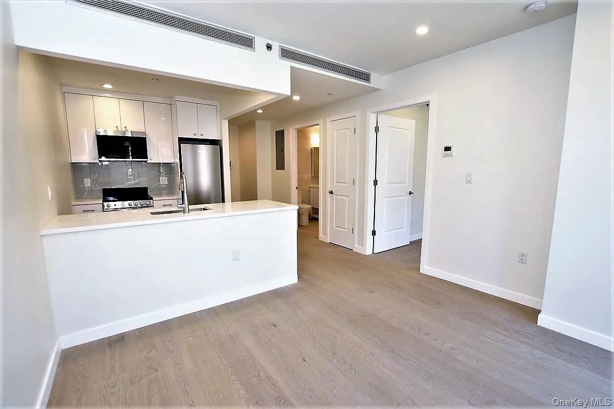 41-26 44th Street, Unit 3C Queens, NY 11104 - Photo 7 of 26 Kitchen with white cabinets, a peninsula, backsplash, appliances with stainless steel finishes, and light wood finished floors