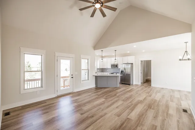 an empty room with wooden floor chandelier and windows