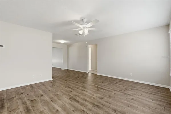 an empty room with wooden floor fan and windows