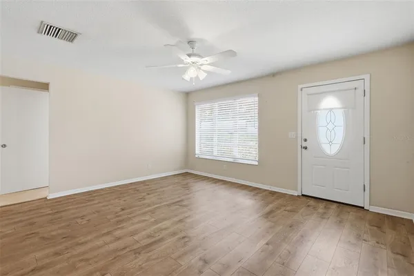 an empty room with wooden floor fan and windows