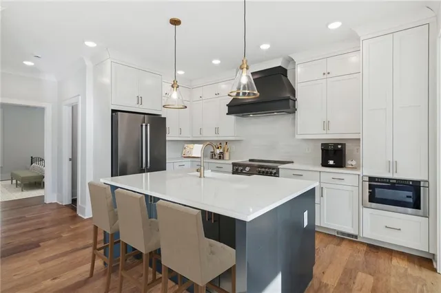 a kitchen with stainless steel appliances granite countertop a stove a sink a refrigerator a microwave oven a stove and white cabinets with wooden floor