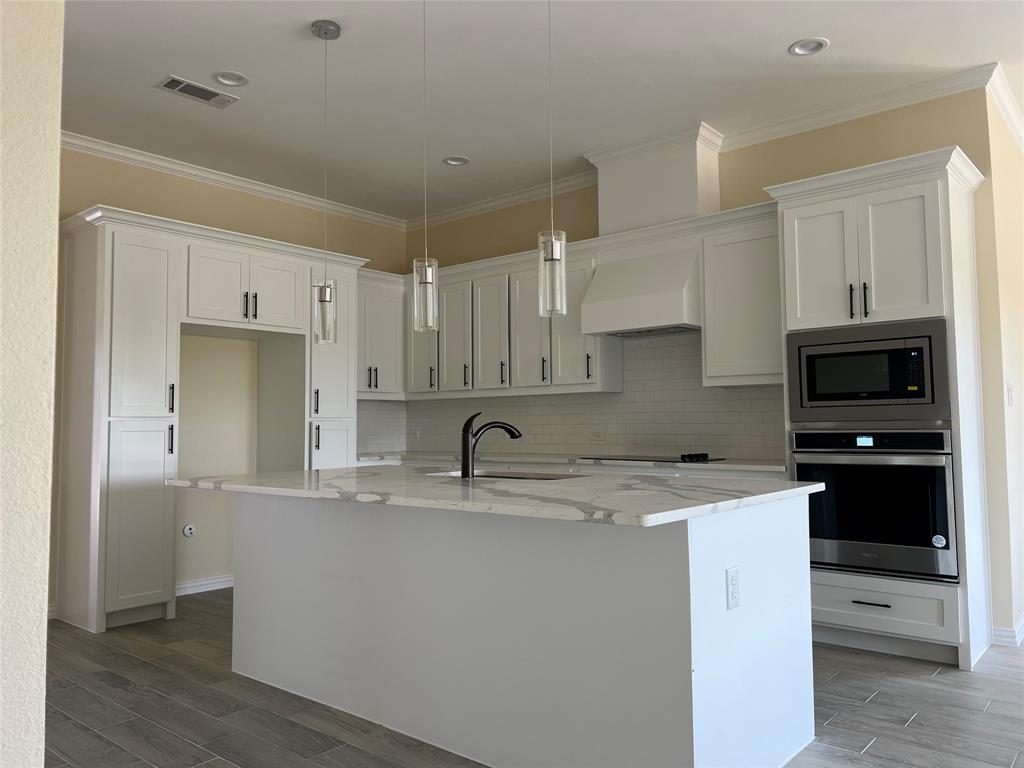 8008 County Road 1058 Rice, TX 75155 - Photo 8 of 25 Modern kitchen featuring a large central island with a light-toned countertop, white cabinetry with dark hardware, a built-in oven and microwave, and wood-finish tile flooring