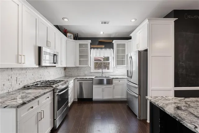 a kitchen with granite countertop a stove a sink and white cabinets with wooden floor