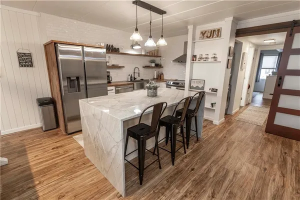 a kitchen with stainless steel appliances granite countertop a refrigerator a microwave a stove and a dining table with wooden floor