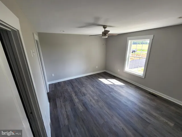 a view of empty room with wooden floor and fan