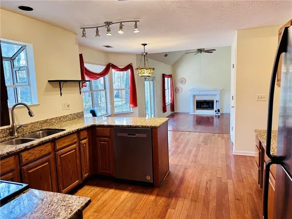 a kitchen with stainless steel appliances granite countertop a refrigerator a sink dishwasher and wooden cabinets with wooden floor