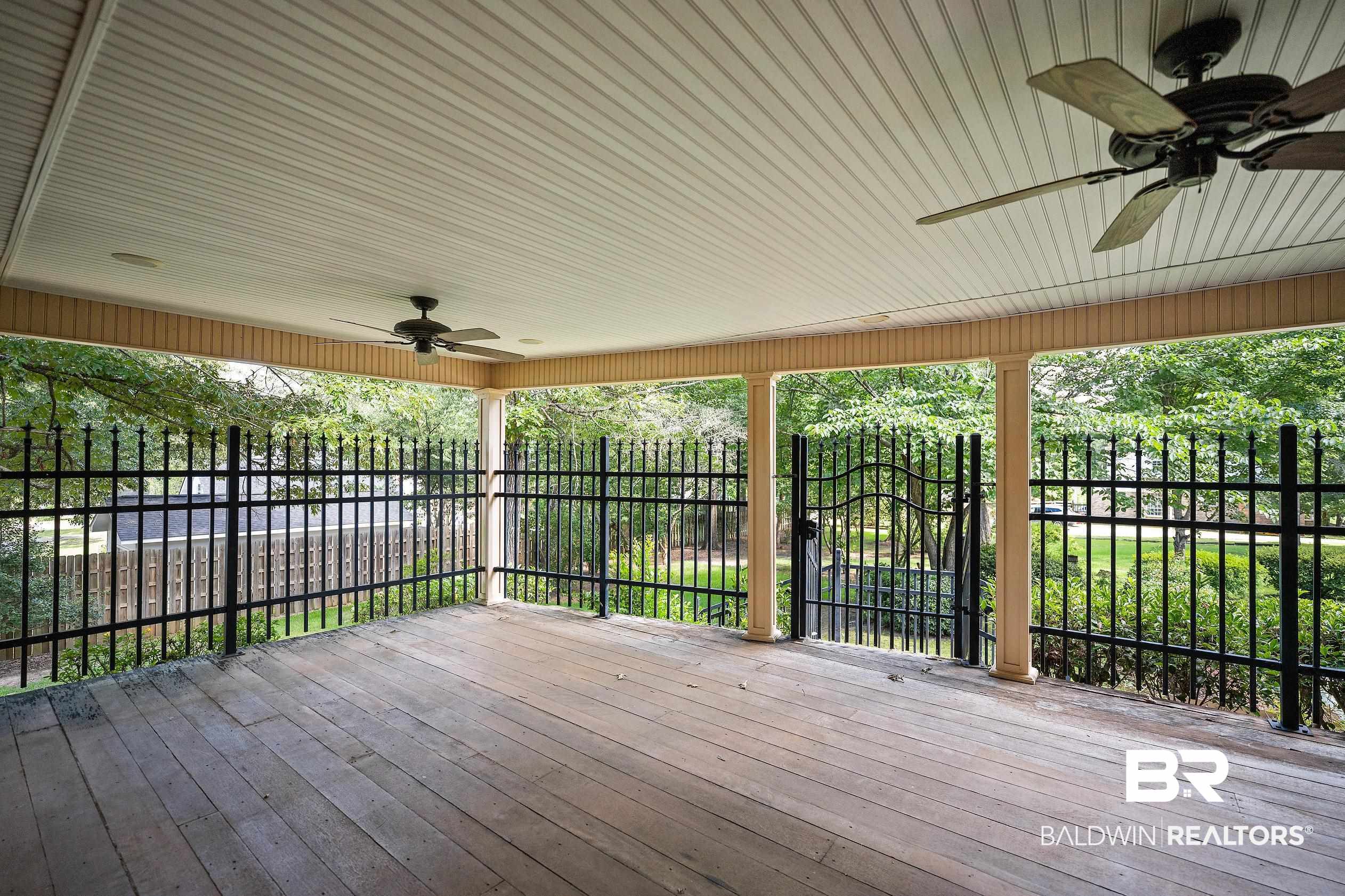 329 Norwood Road Monroeville, AL 36460 - Photo 17 of 49 Spacious covered porch with wood-finish flooring, two ceiling fans, and a black wrought-iron fence