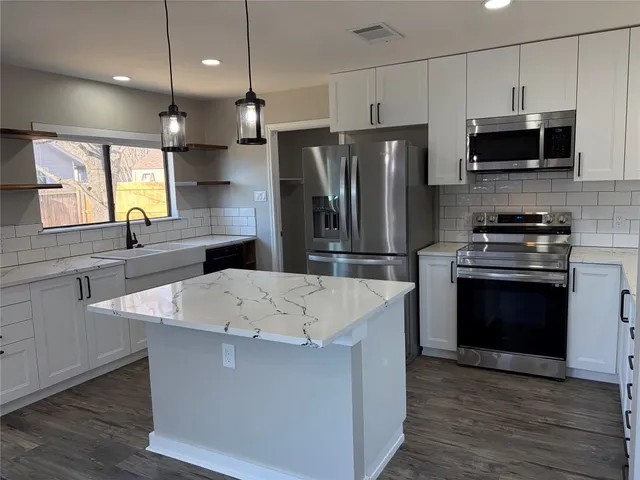 a kitchen with stainless steel appliances a stove a sink a microwave a refrigerator a center island and cabinets