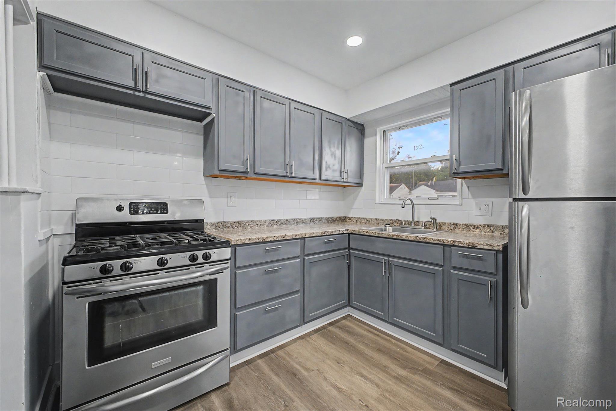 26718 Penn Street Inkster, MI 48141 - Photo 8 of 27 Modern kitchen featuring gray cabinetry, stainless steel appliances, wood-finish flooring, white subway tile backsplash, and stone-finish countertops