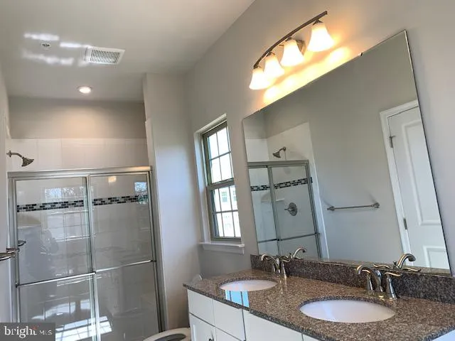 a bathroom with a granite countertop double vanity sink a mirror and a shower