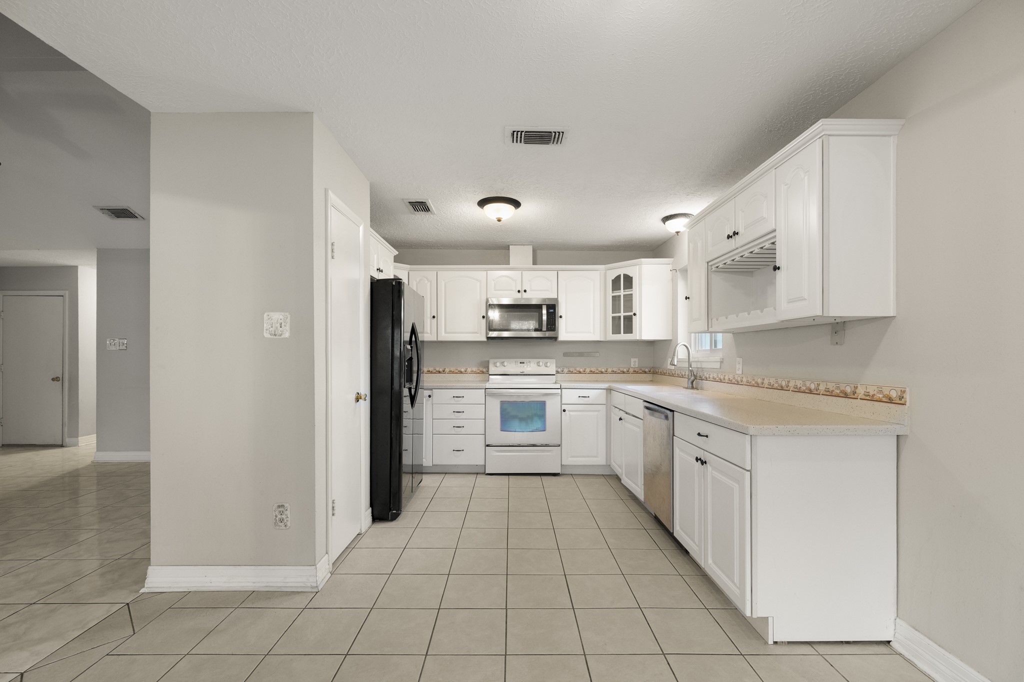 23826 Lestergate Drive Spring, TX 77373 - Photo 5 of 45 Stepping back from the kitchen, this angle gives a broader look at how the space connects to the living room on the left and the breakfast area beyond. White cabinetry, multiple banks of drawers, and the extended counter on the right provide plenty of storage and workspace, while the open layout keeps the kitchen closely connected to the home’s main gathering areas.