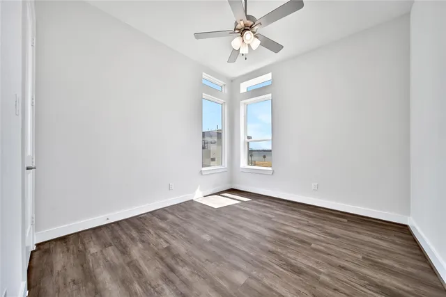 an empty room with wooden floor chandelier fan and windows