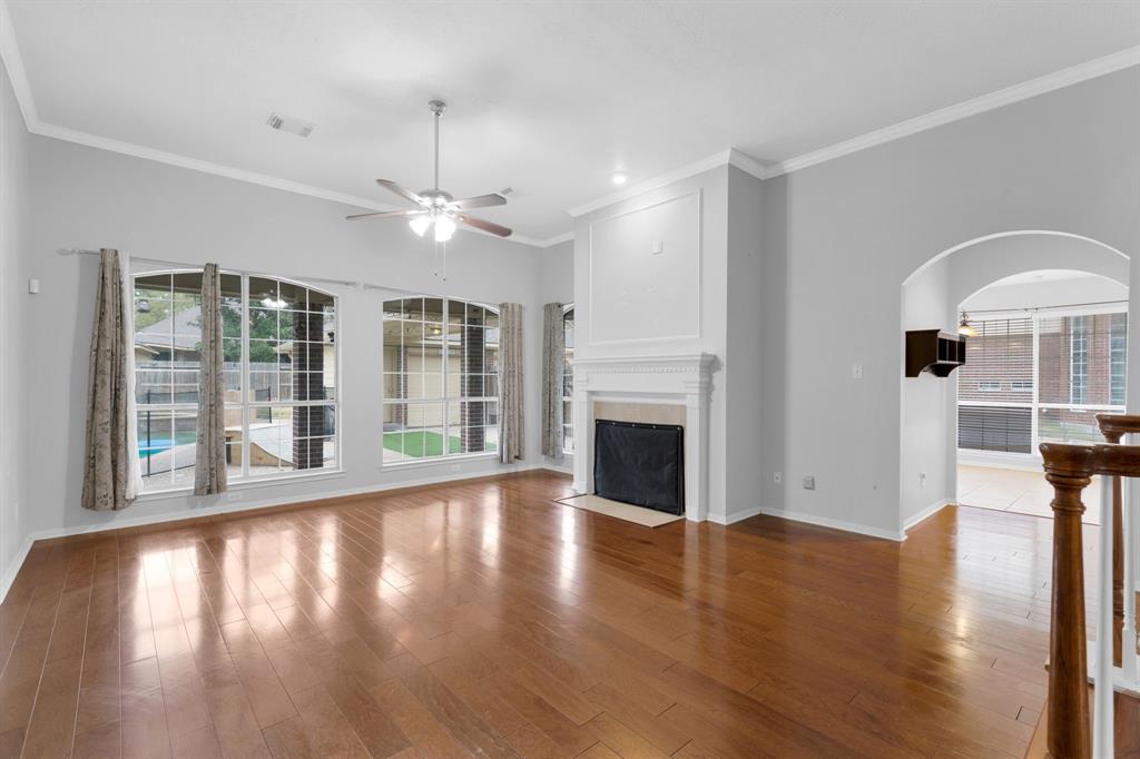3714 Cedar Glen Lane Spring, TX 77388 - Photo 9 of 29 Unfurnished living room featuring arched walkways, ceiling fan, a fireplace with flush hearth, ornamental molding, and wood finished floors