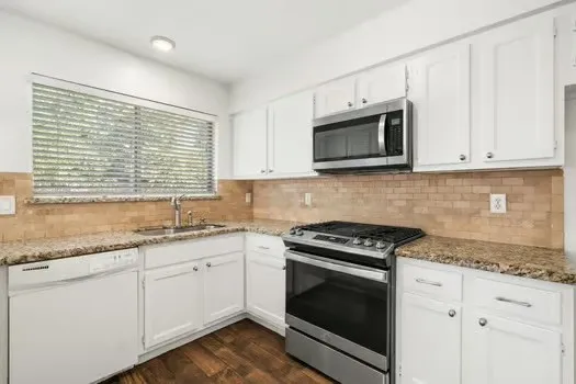 a kitchen with granite countertop white cabinets appliances a sink and a window