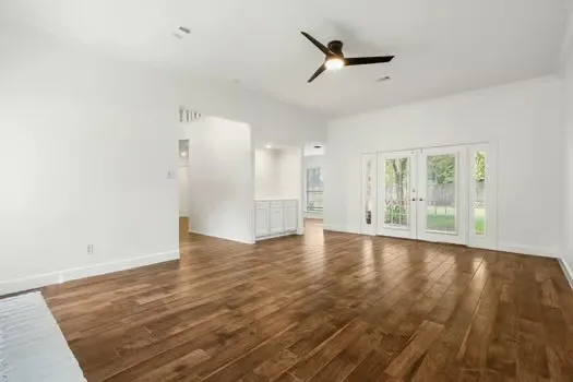 an empty room with wooden floor fan and windows