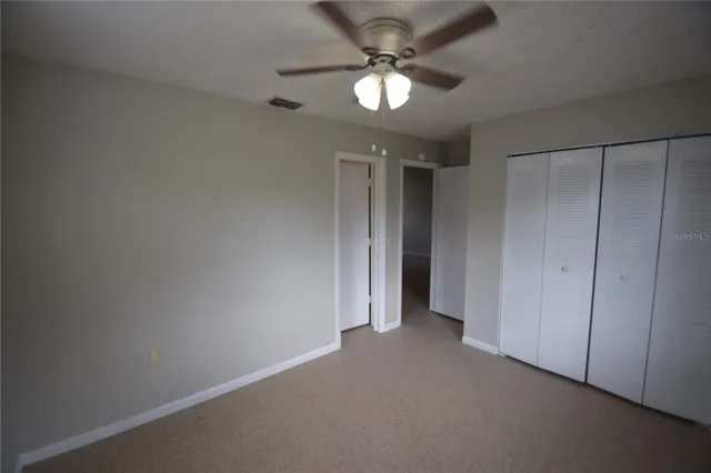 an empty room with a chandelier fan and closet area