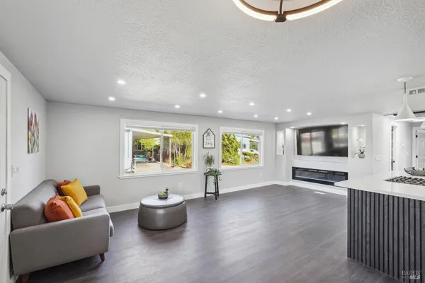 a living room with stainless steel appliances kitchen island granite countertop a stove a refrigerator a sink a dining table and chairs with wooden floor