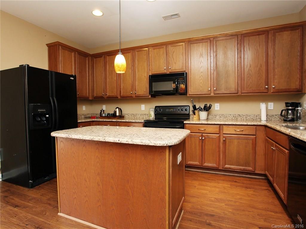 1050 Market Street, Unit 1050 Fort Mill, SC 29708 - Photo 9 of 20 a kitchen with kitchen island granite countertop wooden cabinets and a refrigerator