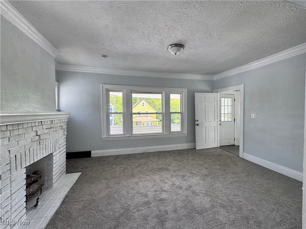 3624 East 118th Street Cleveland, OH 44105 - Photo 29 of 49 Unfurnished living room featuring crown molding, carpet floors, a textured ceiling, and a brick fireplace