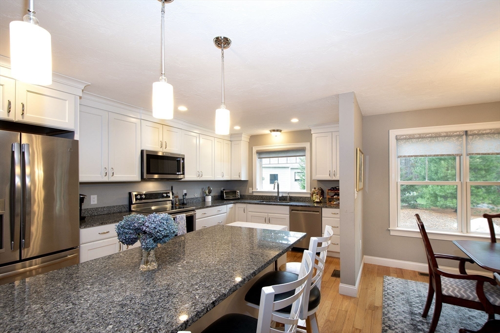 18 Kevin's Way, Unit 18 Scituate, MA 02066 - Photo 7 of 33 a kitchen with stainless steel appliances granite countertop a stove top oven a refrigerator a sink a dining table and chairs with wooden floor