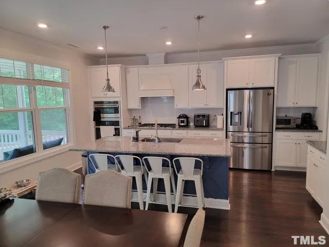 a kitchen with stainless steel appliances granite countertop a refrigerator a sink dishwasher a stove and white cabinets with wooden floor