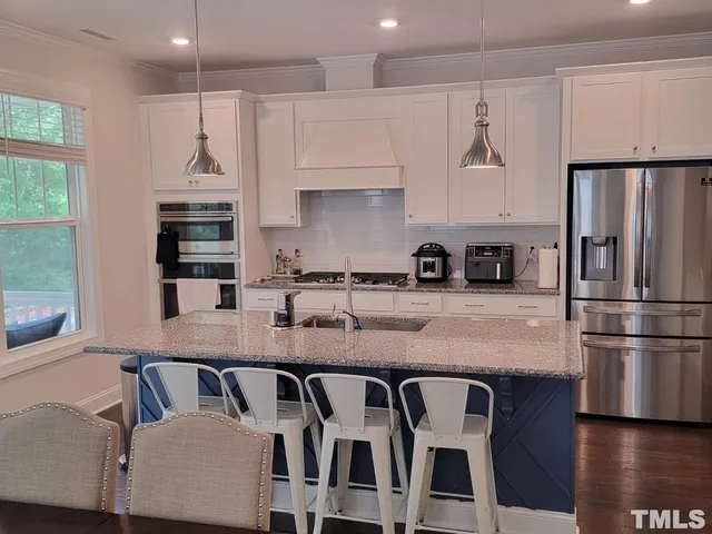 a kitchen with granite countertop a refrigerator a stove a sink and white cabinets with wooden floor