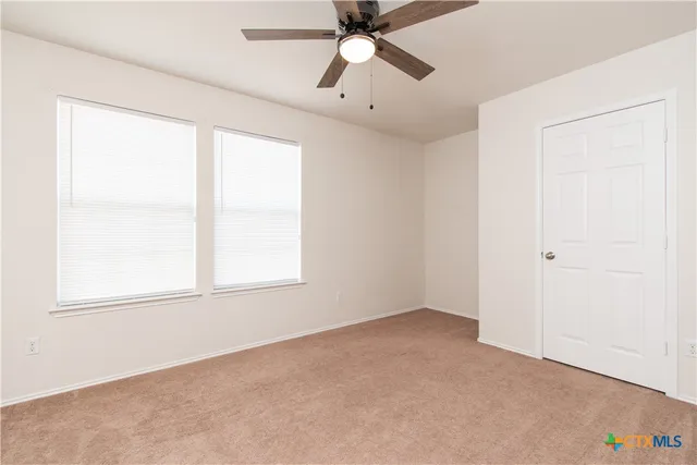 an empty room with chandelier fan and windows