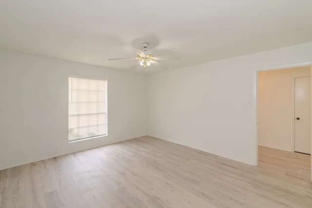 an empty room with wooden floor chandelier fan and windows