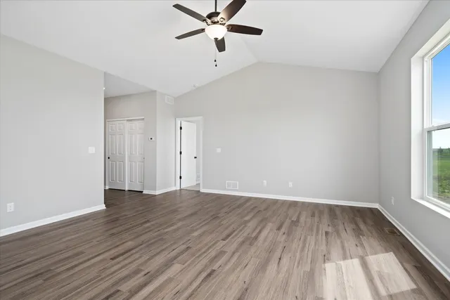 an empty room with wooden floor fan and windows