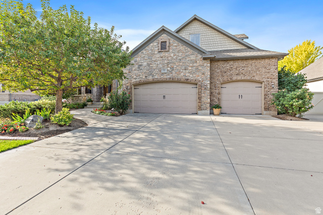Stone and brick exterior with shake siding accents, multiple garage doors, and a concrete driveway